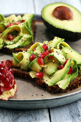 sliced avocado and ripe pomegranates on toast bread with spices and avocado.