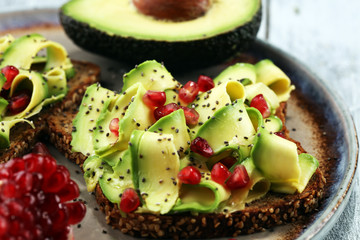 sliced avocado and ripe pomegranates on toast bread with spices and avocado.