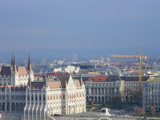 Fototapeta premium View of the Pest side of Budapest, with the Hungarian Parliament on the left side and a construction crane looming over historic buildings in the background