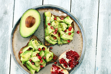 sliced avocado and ripe pomegranates on toast bread with spices and avocado.