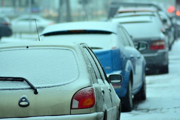 Cars standing in row in traffic jam on city street on slippery snowy road in winter