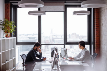 Image of two young Indian and Asian colleagues interacting, sitting opposite each other in office...