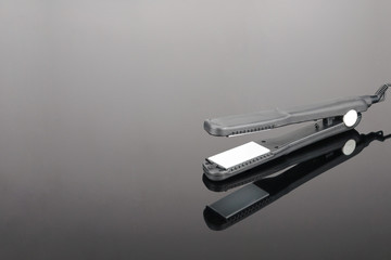 Grey hair iron on the grey mirror background
