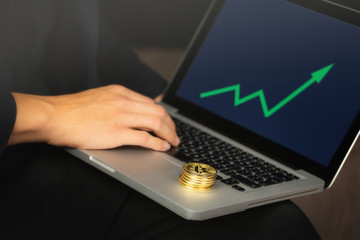 Businessman working on laptop with a golden bitcoin coins stack on it. Green chart, price rise concept.