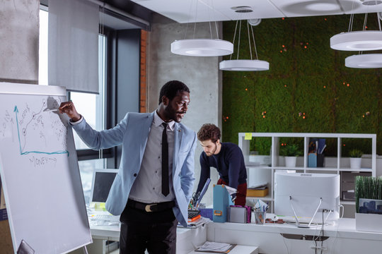 African American lector presenting the successful ideas in front of group of mixed race co-workers people in modern office with loft design and green wall.