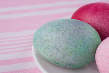 four multicolored painted Easter eggs on a white plate and  striped pink-white tablecloth. holiday easter greeting card, poster, wallpaper