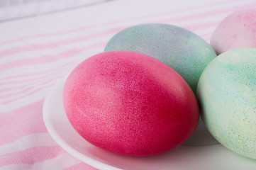 four multicolored painted Easter eggs on a white plate and  striped pink-white tablecloth. holiday easter greeting card, poster, wallpaper
