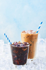 Summer drink iced coffee in a glass and ice coffee with cream in a tall glass surrounded by ice on...