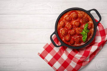 Meatballs in tomato sauce with spices and basil in a frying pan on a white wooden board