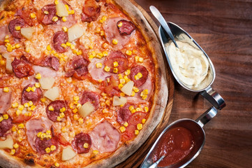 Delicious pizza with sausage, corn and pineapple with white and red sauces. Top view