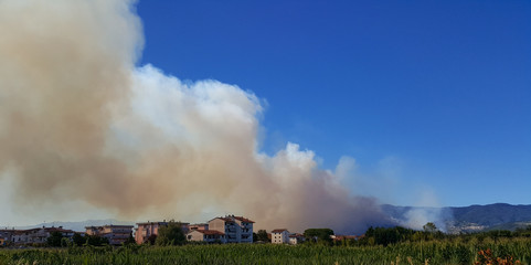 Panoramic fire smoke view on a clear blue sky in a village close to the mountains