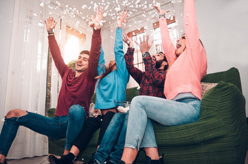 Happy friends at holiday having fun throwing pop corn in the air sitting on the sofa.