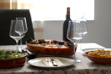 Table setting with four places, roasted vegetables with tomato sauce, salad and mashed sweet potato and wine. Selective focus, moody lighting.