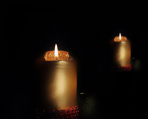 goldene Adventskerze, leuchtend im Spiegelbild mit schwarzem Hintergrund