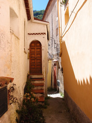 Several steps lead to an old brown door on the street in the city of Maratea, Basilicata, Italy