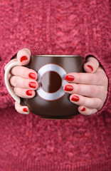 The girl in the red sweater holds a large mug.