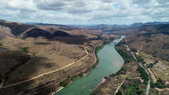 Drone landscape image along the course of the River Doce. Small bridge in the center. In the background mountains and cloudy sky. Atlantic Forest Biome. Video recorded in southeastern Brazil.