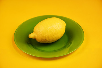 Whole lemon on a glass green plate on a yellow background
