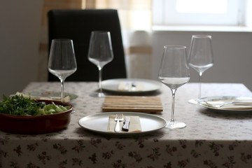 Table setting with four places, salad and wine. Selective focus, moody lighting.