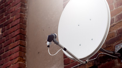 White satellite dish outside on the background of red brick background. Close up of white satellite dish against red brick wall.
