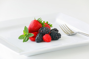 A plate of fresh ripe berries on a white background including strawberries, blackberries, and raspberries