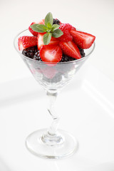 A martini glass full of assorted berries on a white background including strawberries, blackberries, and raspberries