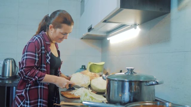 woman in the kitchen preparing a meal concept. girl in the kitchen cuts cabbage with a knife. cook vegetarian food healthy food lifestyle . girl at home in the kitchen slow motion video