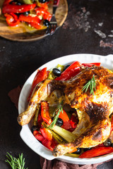 Tasty food: whole roasted chicken with vegetables (red bell pepper, leek  and olives) in a baking dish on a old brown background. 