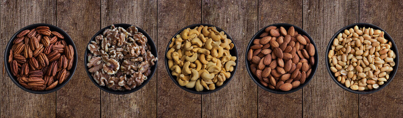 Pekannüsse, Walnüsse, Cashewkerne,Mandelkerne und Erdnüsse in Schüsseln auf Hintergrund aus Holz.