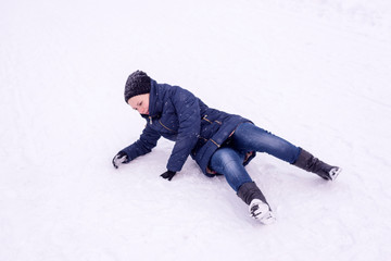 Fototapeta na wymiar The girl slipped on ice covered with snow, falling and injury in the winter
