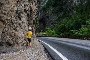 The back of a 6-years blond boy near a rocky mountain and a road