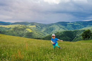 Fototapeta na wymiar lateral view of a 6-years blond boy running on the top of the mountain