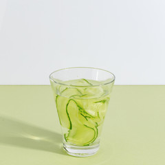 Glass cup with cucumber water on a light green background. Minimalistic creative concept. Copy space.
