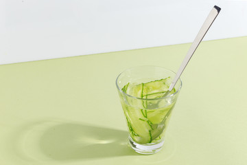 Glass cup with cucumber water on a light green background. Minimalistic creative concept. Copy space.