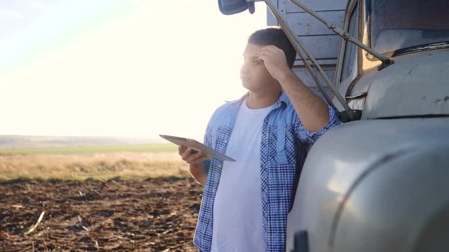 smart farming. man farmer driver stands with a lifestyle digital tablet near the truck. slow motion video. Portrait businessman farmer standing in the field harvesting season car. driver farmer uses a