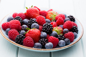 Fresh berry salad on blue dishes. Vintage wooden background.