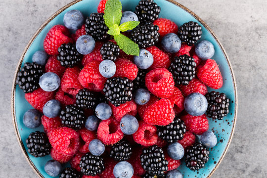 Fresh berry salad on blue dishes. Vintage wooden background.