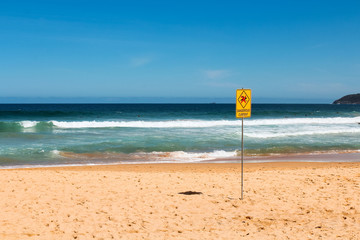 Fototapeta na wymiar Typical Australian yellow dangerous current sign at an empty beach on a clear blue day with waves and white sand (Curl Curl Beach, Sydney, Australia)