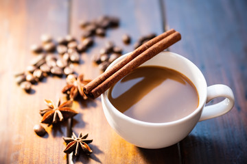 Cup of coffee with cinnamon stick, star anise and roasted coffee beans on wooden table, hot drink