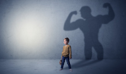 Little waggish boy in an empty room with musclemen shadow behind
