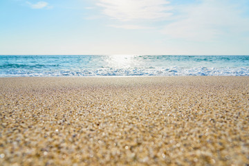 Sandy beach with waves and foam as a natural background with reflection of sunlight on water. Summer holiday concept.