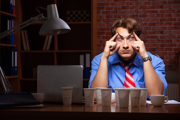 Young employee drinking coffee working at night shift 