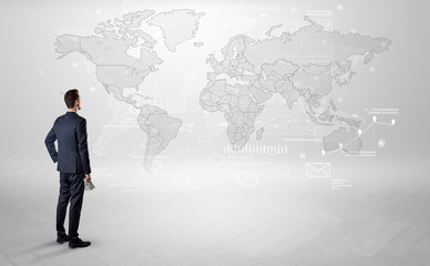 Businessman standing with his back and looking at a worldwide map with objects in his hand
