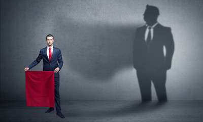 Businessman standing with red cloth on his hand and his shadow on the background
