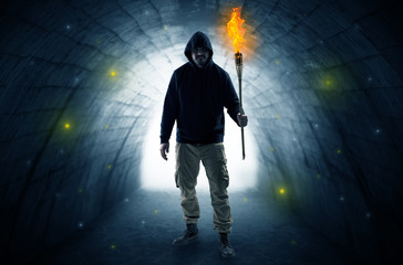 Ugly man with burning flambeau walking in a dark tunnel