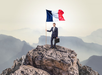 Successful businessman on the top of a mountain holding France victory flag
