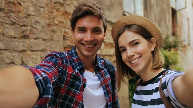 Dating young couple happy in love taking self-portrait photo on a sunny day with a brick wall in the background. Outdoors