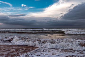 Seashore, stormy sea and colorful clouds on the horizon