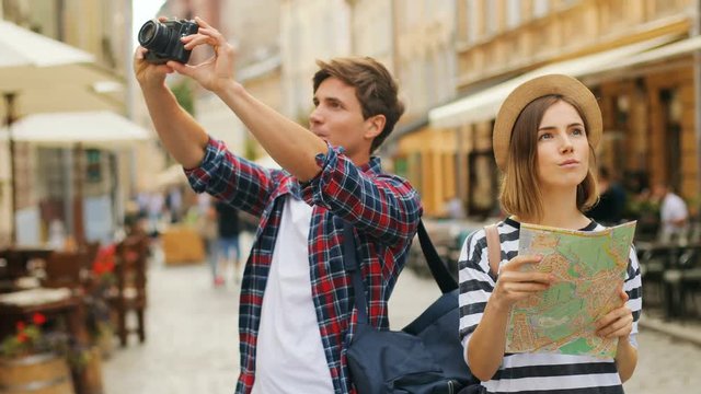 A side view of two happy tourists exploring the city together with a map and taking pictures outdoors.