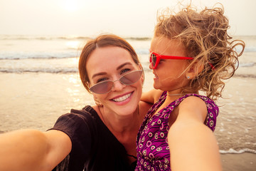 Happy mother and daughter taking selfie photo with smartphone on the Sunset beach. woman having fun with her kid on holiday vacation .Family lifestyle concept.spf and sunscreen